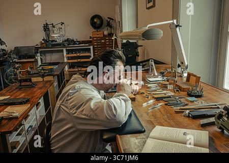 Hervé Schlüchter carefully regulating and cutting a hairspring in his watchmaking atelier, demonstrating the craftsmanship of Swiss horology. Stock Photo