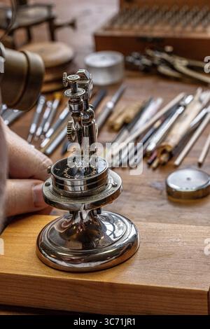 Hervé Schlüchter carefully regulating and cutting a hairspring in his watchmaking atelier, demonstrating the craftsmanship of Swiss horology. Stock Photo