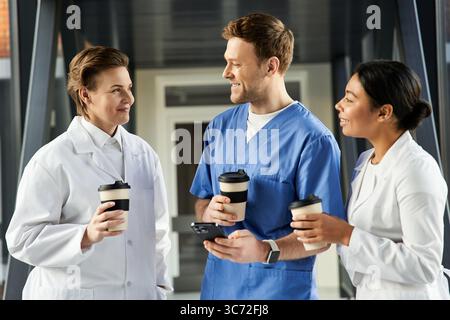 Three diverse medical professionals share a light moment while enjoying coffee together. Stock Photo
