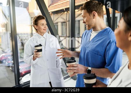 Multicultural medical staff share insights while enjoying coffee in a hospital corridor. Stock Photo