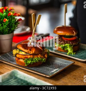 Veggie Burger on a wooden table in a restaurant, meat burger in the background Stock Photo