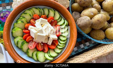 Salad with tomatoes, cucumbers and cheese next to a tray of potatoes Stock Photo
