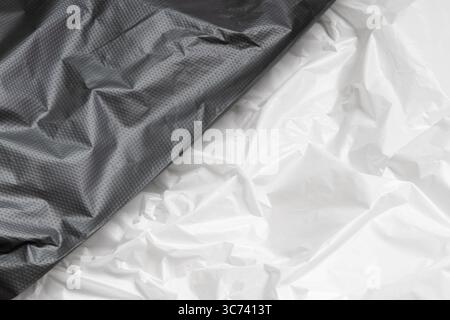 Crumpled black plastic film and white close up, texture of packaging material, plain polyethylene background with highlights and folds for background Stock Photo