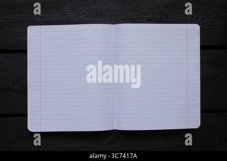 Open school notebook lined on black wooden table and top view, blank pages for notes, used as template or background Stock Photo
