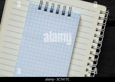 Open notebook in line with white checkered notebook on top, both on spiral, lying on black wooden background and top view, template for notes Stock Photo
