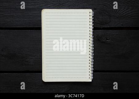 Open lined spiral notebook lies on black wooden background and top view, template for notes Stock Photo