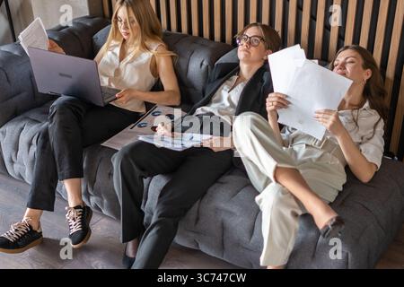 Female business team resting on couch, enjoying a well-earned break in modern office Stock Photo