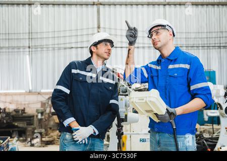 robotics engineers checking a robot arm in an industrial factory Stock Photo
