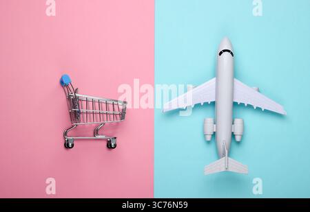 Flat lay composition. Air delivery, shopping, logistics. Figurine of shopping trolley, airplane on blue pink pastel background. Top view Stock Photo