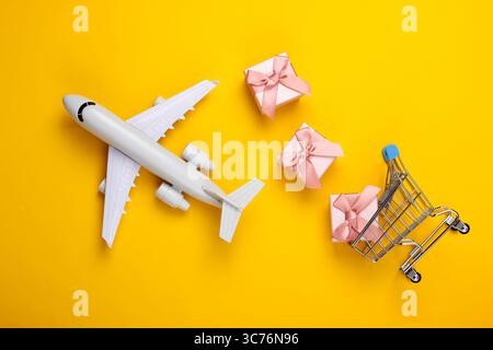 Air delivery. Plane figurine, shopping trolley and gift boxes on yellow background. Flat lay. Top view Stock Photo