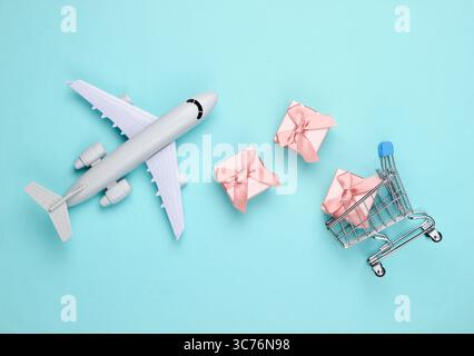 Air delivery. Plane figurine, shopping trolley and gift boxes on blue  background. Flat lay. Top view Stock Photo