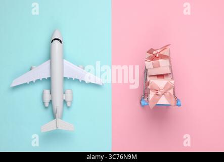 Air delivery. Plane figurine, shopping trolley and gift boxes on blue pink pastel background. Flat lay. Top view Stock Photo