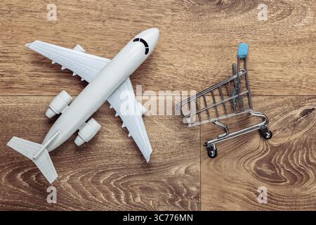 Flat lay composition. Air delivery, shopping, logistics. Figurine of shopping trolley, airplane on wooden floor. Top view Stock Photo