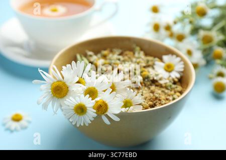 Chamomile flowers in bowl on light blue background, closeup Stock Photo