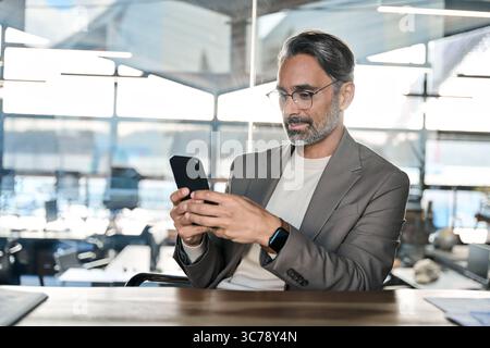 Busy mature business man investor thinking looking at cell phone in office. Stock Photo