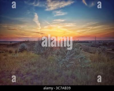 A beautiful sunset over a grassy landscape. The sky is filled with vibrant colors and wispy clouds. Stock Photo