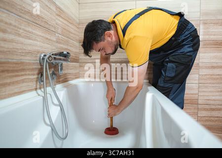 Plumber working to unclog bathtub drain using plunger Stock Photo
