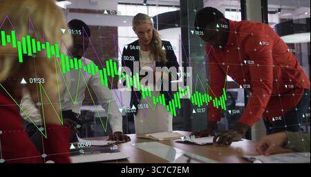 Reviewing businesswoman in black blazer leaning over boardroom table with tablet and data charts Stock Photo