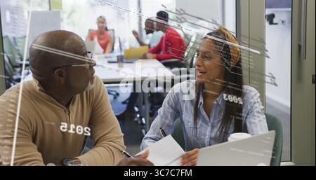 Sitting senior man in sweater and woman with headband discussing project at office, with laptop Stock Photo