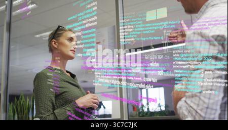 Professionals analyzing colorful projected code in conference room, with marker on glass partition Stock Photo