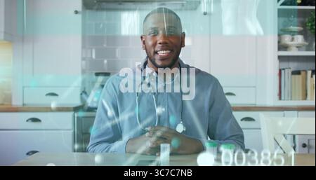 Smiling doctor wearing blue shirt with stethoscope showing pills at kitchen table, medical concept Stock Photo