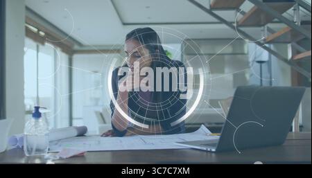 Reviewing female architect leaning over blueprints at modern home office, with sanitizer dispenser Stock Photo