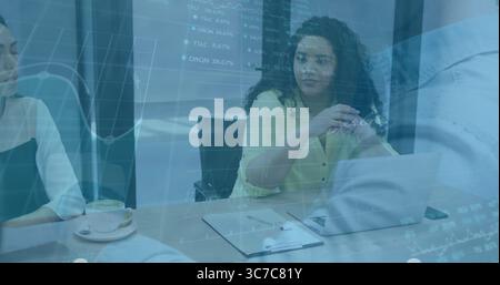 Woman in yellow blouse leading meeting in conference room, with laptop clipboard and stock charts Stock Photo
