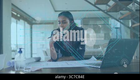 Leaning woman in blazer reviewing blueprints on desk in modern office, holding smartphone and pen Stock Photo