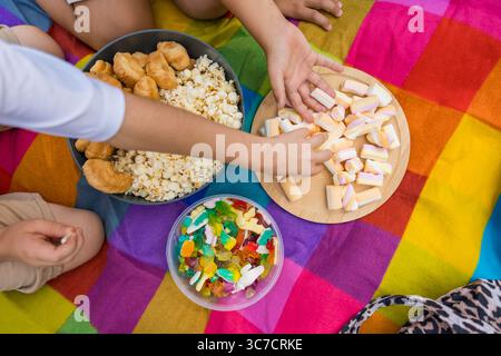 Childrens hands reaching for sweets during colorful picnic on rainbow blanket Stock Photo