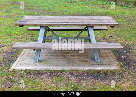 Photograph of a fixed in place reasonably well maintained family sized wood and steel picnic table with adequate seating located in a public park. Stock Photo