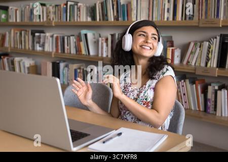 Carefree student woman in headphones listening music seated at table Stock Photo