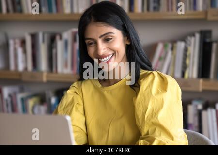 Cheery Indian woman reading pleasant news on laptop and laughing Stock Photo