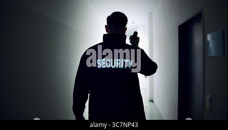 Night Warehouse Security Guard Patrols In Uniform With Flashlight, Providing Safety Stock Photo