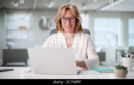 Experienced Businesswoman Focused On Laptop In Home Office Setting. Stock Photo