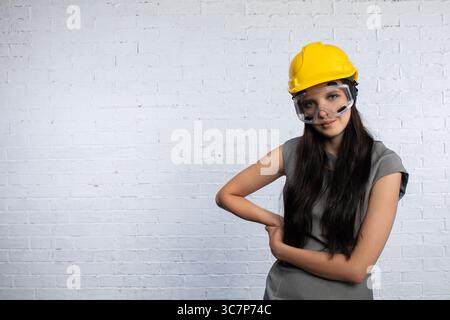 A young woman dressed in construction gear, complete with a safety helmet, stands confidently Stock Photo