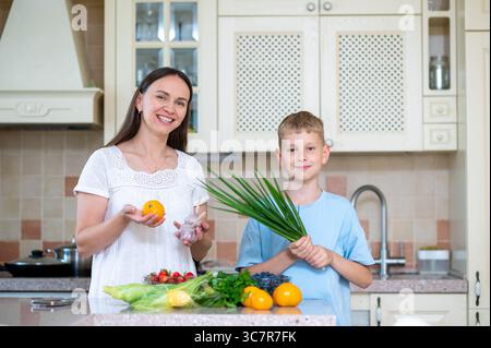 Woman and boy show green onion and tomatoes together. Concept of teaching kids healthy eating through family lifestyle Stock Photo