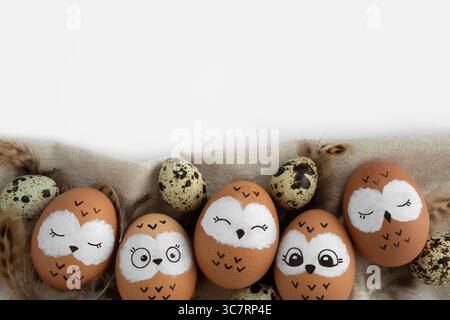 Funny owl family. Brown easter eggs with painted faces, quail eggs and bird feathers. Space for your text. Stock Photo