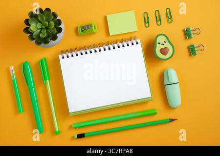 Empty page with green pen, pencil and marker on yellow background. Eraser in the form of avocado. Flatly. Stock Photo