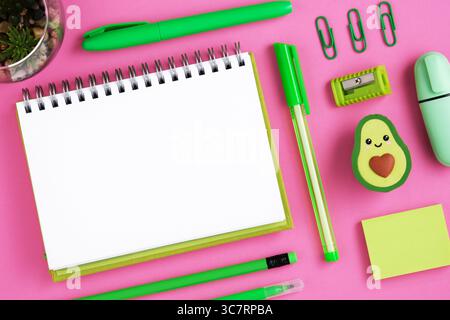Blank notepad sheet with green school and office stationery on pink background. Eraser in form of avocado. Flatly. Stock Photo