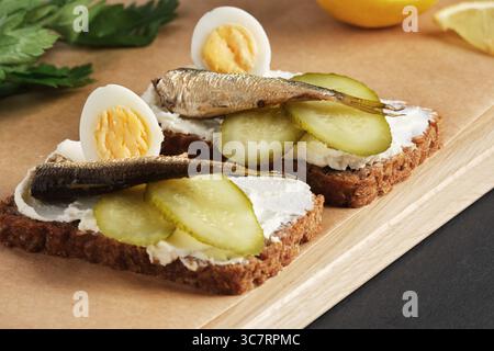 Sandwiches with sprats, quail eggs, pickles on wooden serving tray on black stone background. Stock Photo