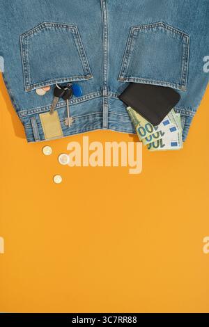 Wallet, bills, coins and keys fly from the back pockets of blue jeans. Yellow background, place for your text. Stock Photo