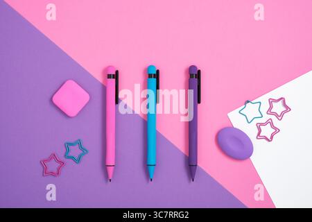 Stationary background with bright magenta, cyan and violet pens, clips and erasers on pink, and purple backdrop. Stock Photo