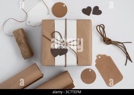 Craft gift box, wrapping paper, twine, gift tags and wooden hearts on a white background Stock Photo