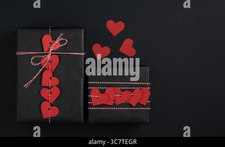 Two black gift boxes with garland of red hearts on black background. Space for your text. Present for Valentine's Day Stock Photo