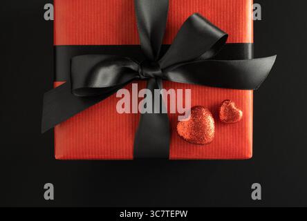 Part of gift box with red bow and two red shiny hearts on black background. Present for Valentine's Day. Stock Photo