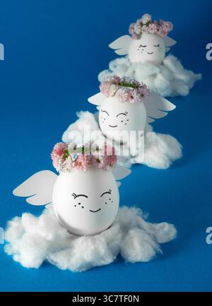 Angels made of eggs in flower wreaths on the clouds. Decorated Easter eggs. Blue background. Stock Photo