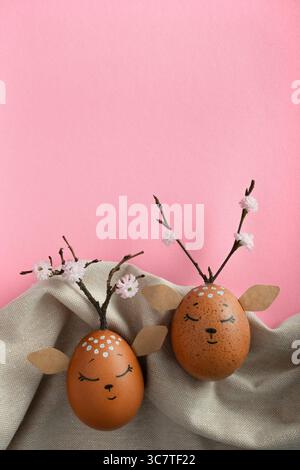 Two sleeping deers made of eggs on fabric background. Brown Easter eggs, quail eggs. Space for your text. Pink background Stock Photo