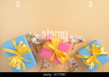 Pink and blue gift boxes with yellow ribbons on pastel yellow background with white apple flowers. Horizontal, space for text. Stock Photo