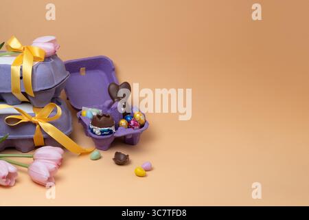 Sweet Easter gifts in a purple egg box on pastel yellow background. Horizontal, copyspace. Stock Photo