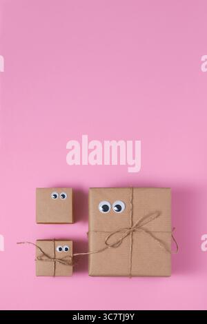 Card with brown craft gift boxes with eyes on pink background. Space for your text, vertical. Stock Photo